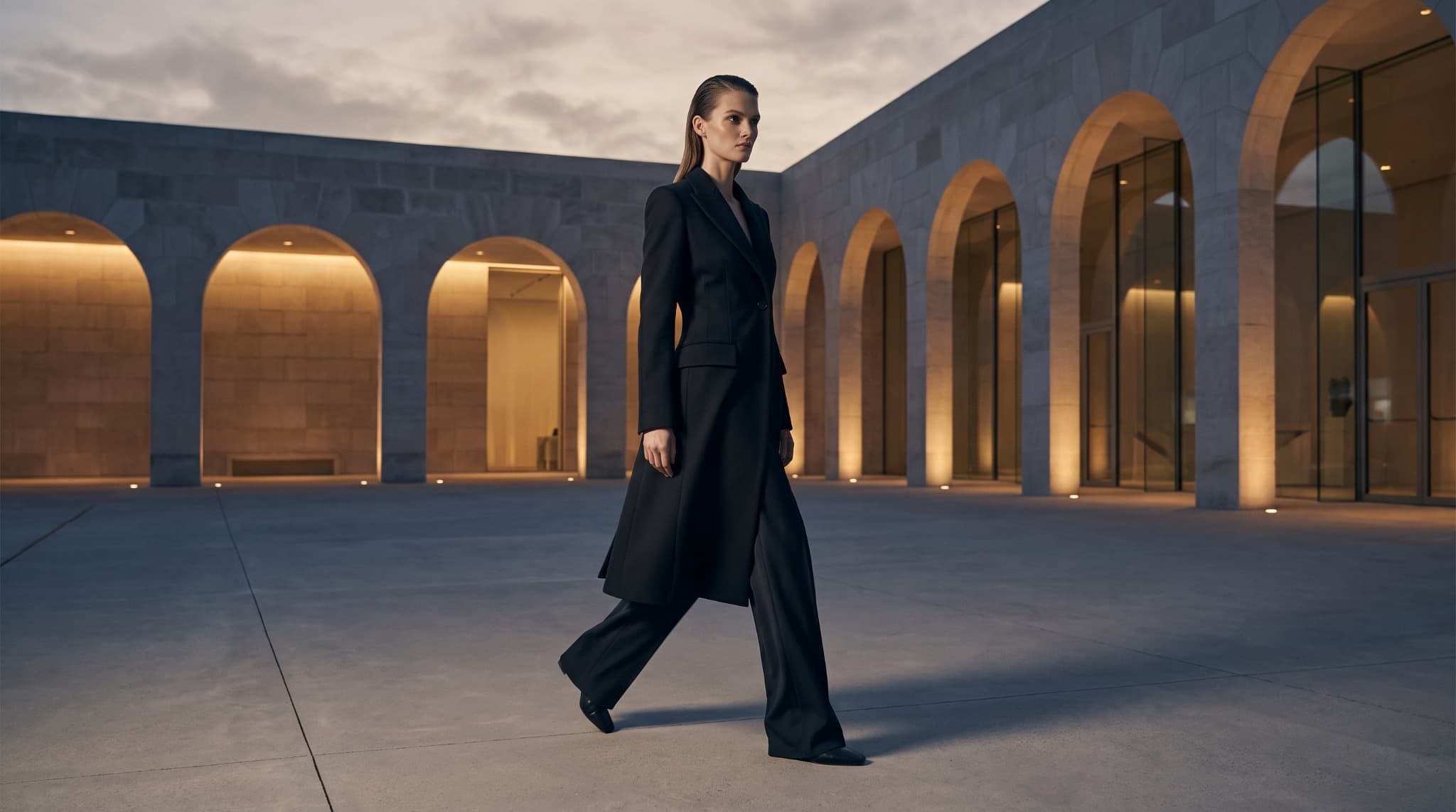 Model crossing a modern courtyard in a black editorial look